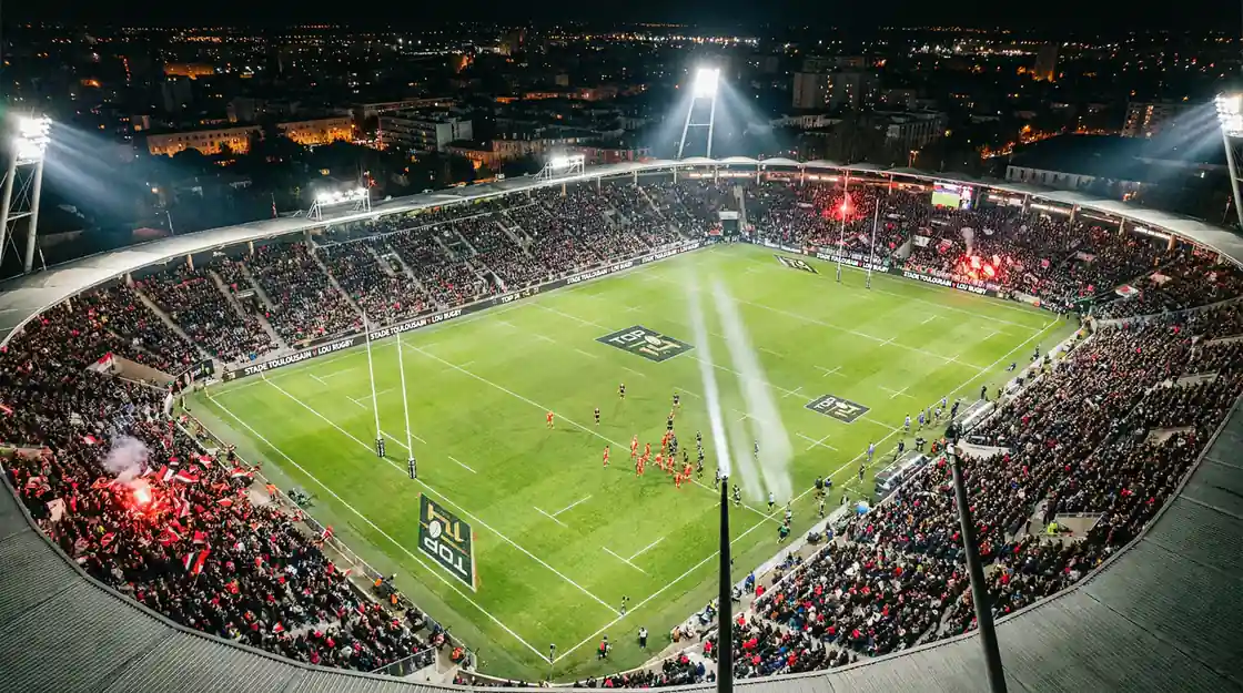 Stade de rugby français illuminé lors d'un match du Top 14, vue aérienne du terrain